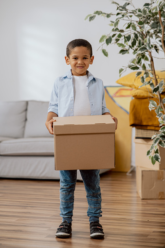 A little boy helps his parents move he holds a small cardboard box in hands carries it to a new room, selling an apartment, renting a house