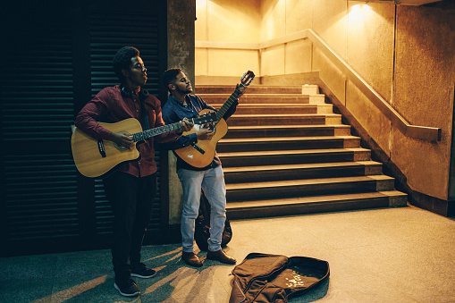 Two Afro-American playing acoustic guitars and singing in the entrance hall of the subway corridor and receiving money for it.