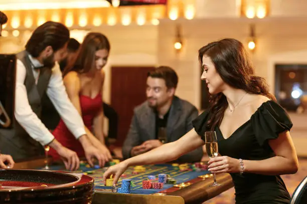 A young brunette woman in a dress sitting at table roulette playing poker at a casino.