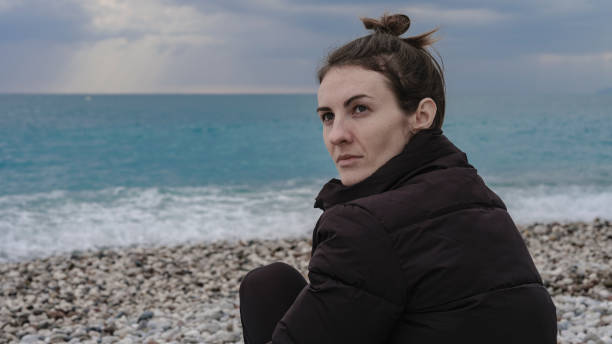 istock beautiful woman sitting alone on the beach 1364020135