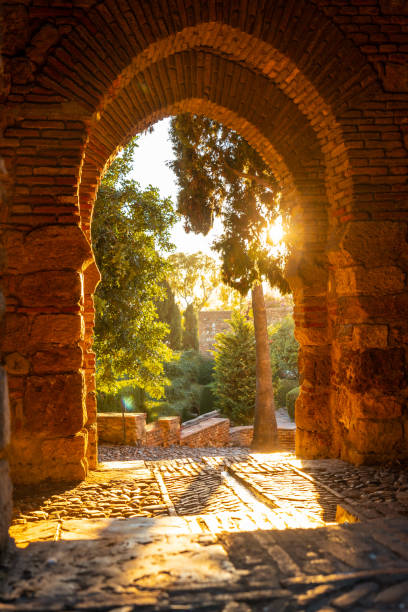 壁の門とマラガ、アンドラルシアの街のアルカサバの庭園の夕日。スペイン。アラビア語スタイルの中世の要塞 - alcazaba ストックフォトと画像