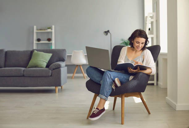 istock Smiling woman sitting at home with laptop and making notes during online lesson 1364022732