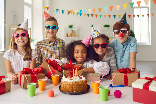 portret afroamerykańskiej solenizanty z przyjaciółmi, którzy siedzą przy stole z prezentami. - kids birthday party zdjęcia i obrazy z banku zdjęć