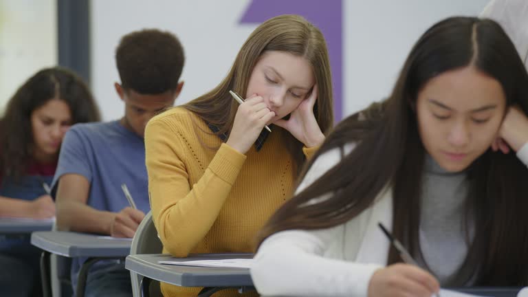 Junior high students taking exam at desks in classroom