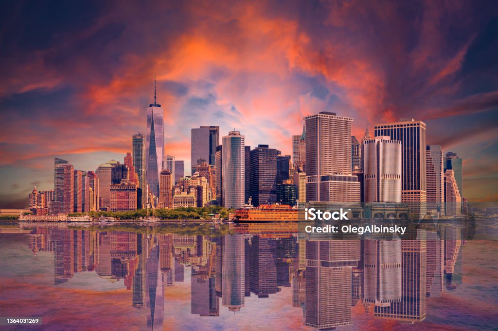 New York City Skyline with Manhattan Financial District, World Trade Center and Orange and Blue Sunset Sky. New York City Skyline with Manhattan Financial District, Battery Park, World Trade Center, Sail Boat, Staten Island Ferry and Dramatic Orange and Blue Sunset Sky with Clouds All Reflected in Water of New York Harbor, Canon EOS 6D Full Frame Sensor Camera and Canon EF 24-105mm f/4L IS USM Lens. New York City Stock Photo