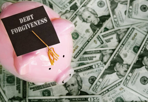 Piggy bank with Debt Forgiveness graduation cap on cash stock photo