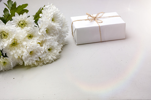 bouquet of white chrysanthemums and a gift box on a concrete background with light highlights, selective focus