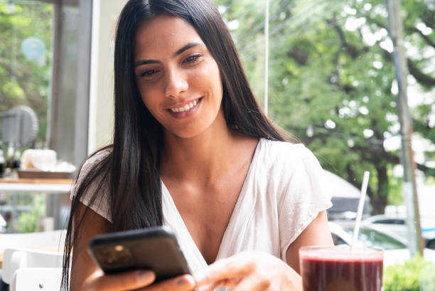 istock Mexican mid adult woman text messaging while sitting having a smoothie 1364034135