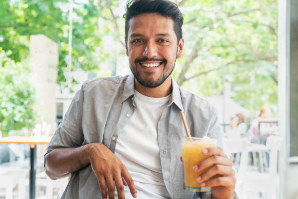istock Smiling young latin man looking at the camera holding cold drink 1364034140
