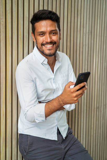 istock Cheerful latin male holding smartphone while looking at the camera 1364034417