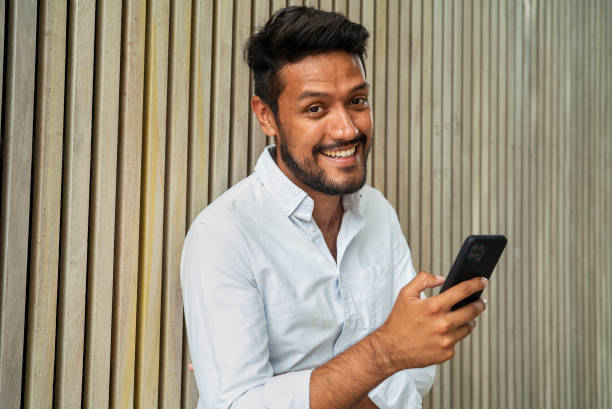 istock Cheerful latin male holding smartphone while looking at the camera 1364034443
