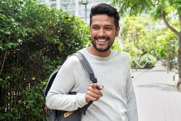 istock Mexican man standing on sidewalk while smiling and holding backpack on shoulder 1364035680