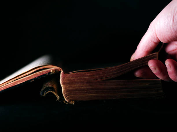 istock Hand opening an old worn book on dark background 1364037836