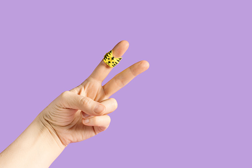 Fingers peace sign wearing origami paper ring with tiger face against pastel background. Minimal Chinese New Year festive celebration concept.