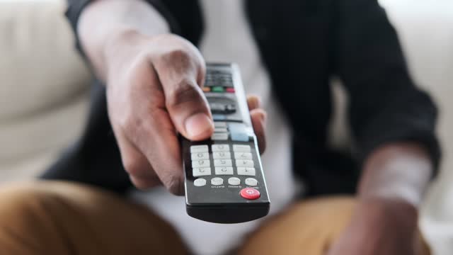 Male hand using remote control to switch channels on television
