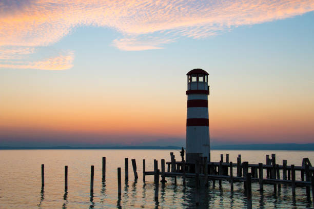 istock Low horizon romantic sunset sky over the lake landscape with red white lighthouse architecture and dock pillars in the water, beautiful warm colours of the largest lake in Central Europe, Neusiedl See 1364053920