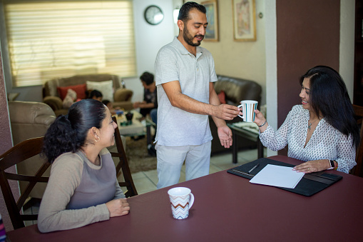 Couple at home with advisor, grandparents playing with grandchildren in the background