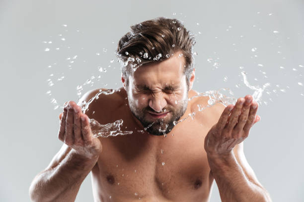 istock Young man standing isolated over grey background washes face. 1364057332