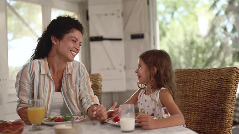 Happy single mother talking to her girl during breakfast at home.