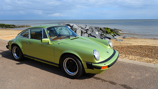 Felixstowe, Suffolk, England - May 05, 2019: Classic Green Porsche motor car parked on seafront promenade sea in background.