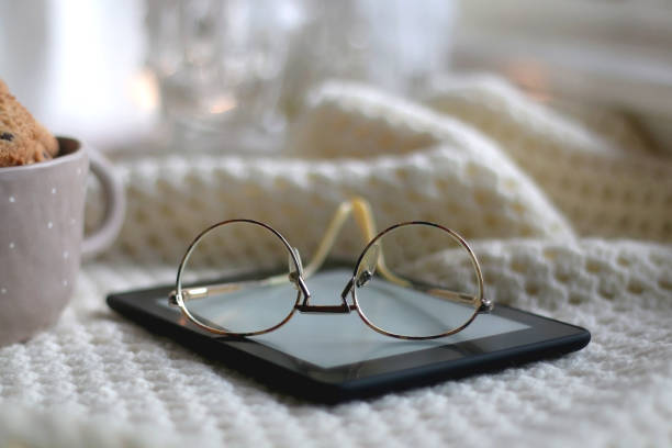 Tablet, Glasses, Cookies and Blanket Bowl of chocolate chip cookies, digital tablet, reading glasses, soft blanket and lit candle. Hygge at home. Selective focus. reading glasses stock pictures, royalty-free photos & images