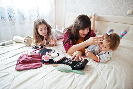 Mother and daughters doing makeup on the bed in the bedroom.