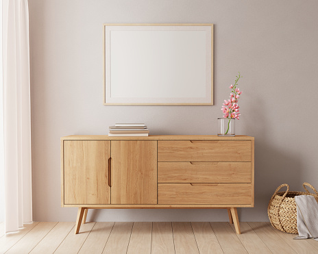 Living room interior with brown chest of drawers, stack of books, pink flower and round wicker basket. Picture mock up on warm, sepia wall. 3D render.