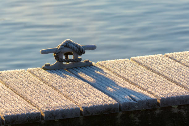 Gray mooring line with hoarfrost A gray mooring line attached to a bollard cleat on the edge of a frozen jetty in the backlight of an early winter sun. mooring line stock pictures, royalty-free photos & images