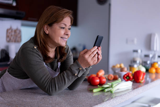 istock Beautiful mature woman leaning her elbows on kitchen counter while looking for an online recipe on smartphone at home 1364071222