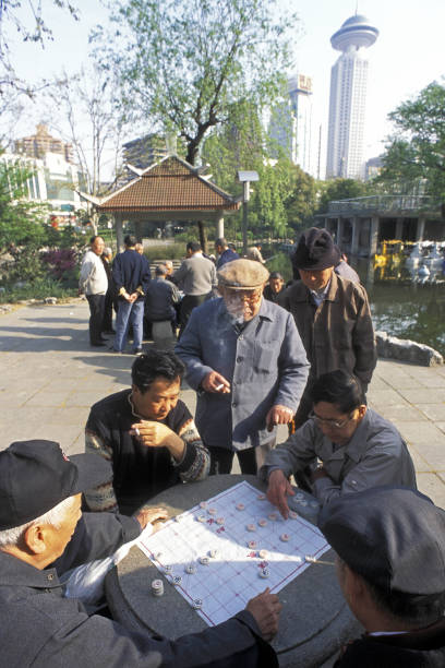 gli uomini anziani giocano a un gioco da tavolo nel people's park, uno dei parchi cittadini più belli della città, situato a sud di nanjing lu road con il grattacielo sullo sfondo, shanghai - peoples park foto e immagini stock