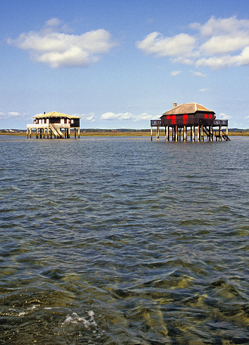 Fishermen's stilt huts in shallow water, Bay of Arcachon,, Aquitaine, France. Situated in Pays de Buch between the Côte d'Argent and the Côte des Landes, in the Aquitaine region, the bay is extremely shallow and covers an area of 150 square kilometres (60 sq mi) at high tide and square kilometres (15 sq mi) at low tide. France enjoys many quaint and historic towns and villages both coastal, on its islands and inland with beautiful architecture and historic detail such as stone carving, half timbered building construction and cobbled streets