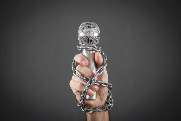 istock Human hand holding microphone tied with chains. 1364072799