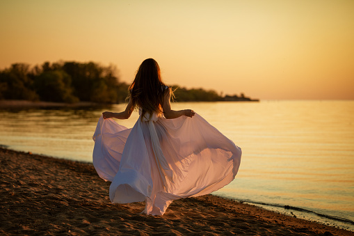 Young free woman running in white dress near the sea at sunset