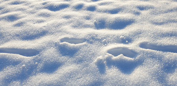 Full frame freshly fallen frozen snow, shiny crystals and deep footsteps in snow.