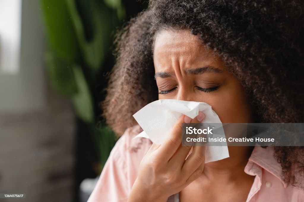 Sneezing coughing ill young african woman using paper napkin, having runny nose, blowing her nose. Coronavirus, infectious disease, flu, cold. Allergy Stock Photo
