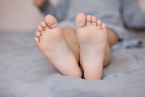 A girl in a gray dress holds children's feet on a gray blanket. Little girl's legs.