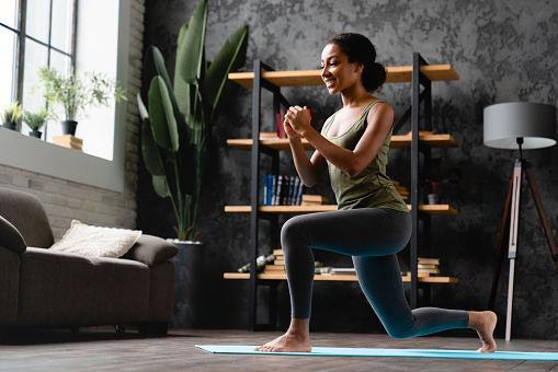 Slimming and healthy active lifestyle. African young female athlete woman teenage girl stretching on fitness mat, training her body at home