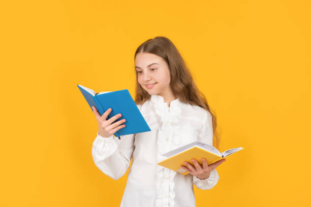 istock cheerful child reading school book on yellow background, school 1364076978