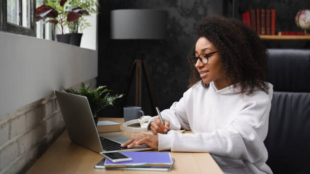 afrykański młody nastolatek e-learning na odległość, korzystanie z laptopa, pisanie zadań domowych w zeszycie, oglądanie webinariów online z domu. - learning education internet university zdjęcia i obrazy z banku zdjęć