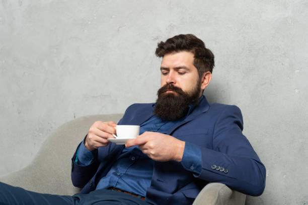 もう一杯のリラックスしたお茶。マネージャーの男性は、アームチェアでリラックスしたコーヒーを飲みます。職場での休憩 - content businessman executive director manager ストックフォトと画像