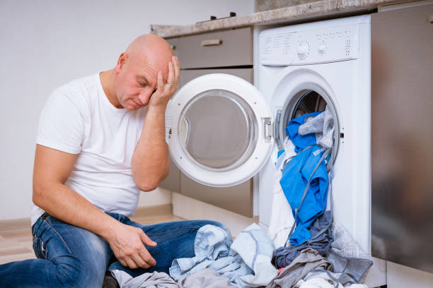 istock tired man sits with laundry at the washing machine 1364084689