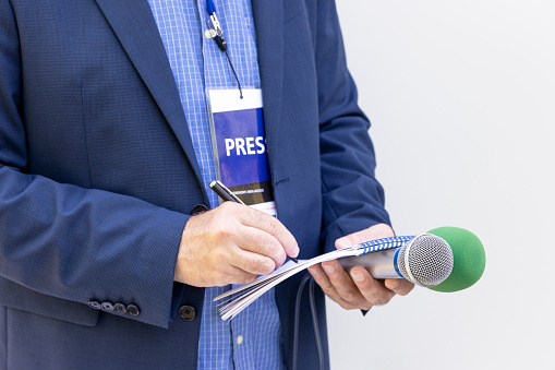 Reporter at press conference or media event, holding microphone, writing notes. Journalism concept.