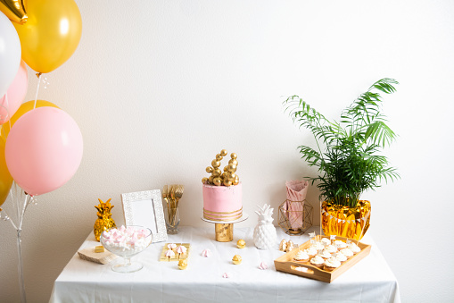 Holiday birthday table with cake and ballons. Pink and golden decoration for celebration with palm. Copy space