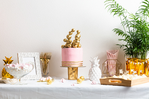 Holiday birthday table with cake and ballons. Pink and golden decoration for celebration with palm. Copy space