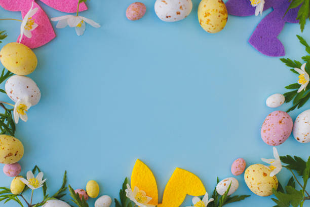 istock Colorful Easter bunnies, chocolate eggs and spring flowers frame on blue background, flat lay with space for text. Happy Easter! Pink and yellow artificial decor and fresh flowers. Easter hunt 1364090020