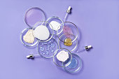 istock Cosmetic products, scrub, face serum and gel in many petri dishes on a pink background. Cosmetics laboratory research concept. Pastel violet background 1364090950