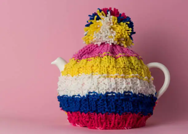 Teapot with a knitted coat on a pink background