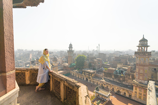 Young Caucasian female tourist in hijab standing near the minaret and looking at Lahore city from above