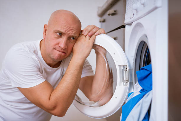 istock tired man sits with laundry at the washing machine 1364094687