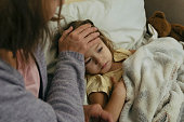 Portrait of sad engrossed sick little girl and her mother touching daughter's forehead.
